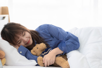 Young Asian woman sleeping and hug teddy bear on white bed and have a night dream.