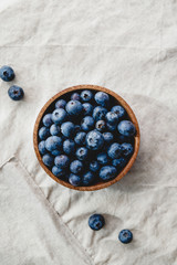 Fresh blueberry in a wooden bowl on a linen light cloth. Healthy eating and Summer concept.