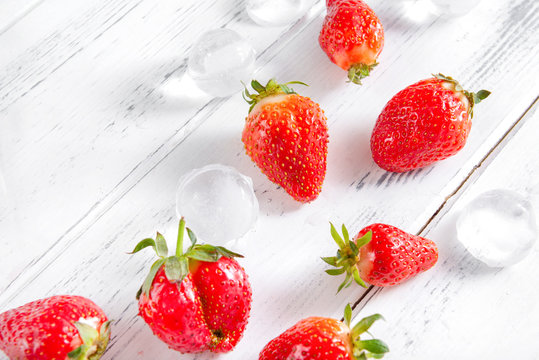 few red ripe strawberries with ice cubes on a white wooden background