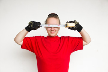 Fototapeta na wymiar happy girl in red t-shirt and black gloves covers her eyes with a building tape and smiles on the white wall background, female agricultural worker, free space