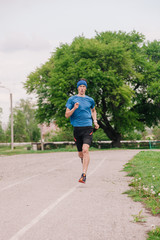 Fototapeta premium A young athlete in a blue T-shirt runs around the stadium