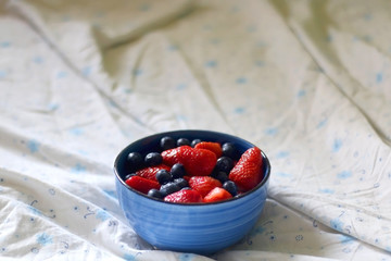 Bowl of blueberries and strawberries on a bed. Selective focus.