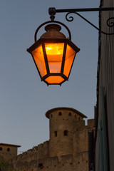 Fototapeta na wymiar Vintage Street light lit at dusk in Carcassonne, France. Walls of the fortified city in in the background