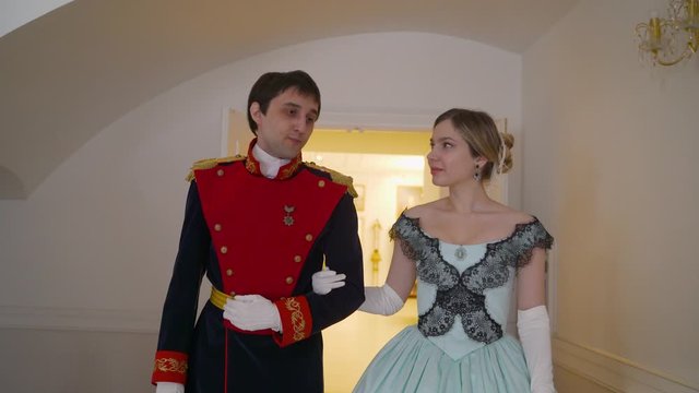 The guy in uniform invites the girl to dance. Love story guy invites a girl in an old, beautiful dress to dance. A guy and a girl in clothes from the 19th century.