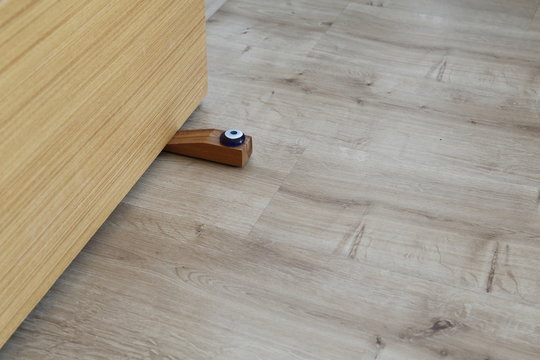 Close-up elements of the interior of the apartment. Wooden chrome door stopper on laminate floor