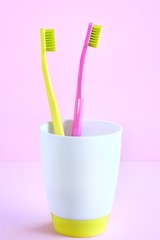 Bright plastic toothbrushes in bathroom glass on neutral pink background, selective focus. New toothbrush for personal hygiene. Healthcare concept. Caries Prevention. Dental care. Vertical position 