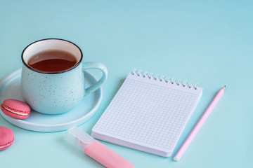 Home office desk workspace with notebook, marker and cup of black tea with macaroons on blue background. Workplace for freelancer or blogger. Work concept. Copy space
