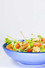 Chicken salad with tomatoes, pear and green salad on the blue bowl, white background.