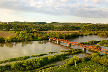 Fototapeta na wymiar Aerial view of a narrow road bridge stretching over muddy wide river in green rural area.
