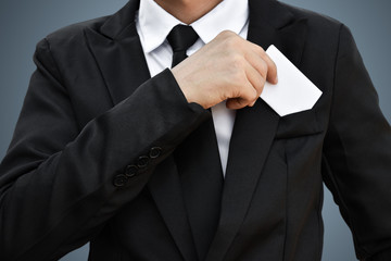 Closeup of businessman who takes out white piece of paper from the pocket in black suit. Idea for business credit card or visiting card.