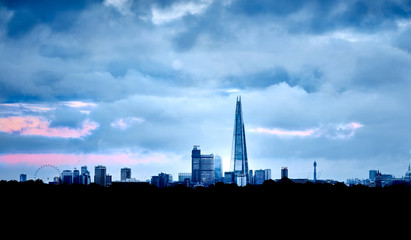 City skyline at dawn. This photo of London has the first glow of the sun rising up through the skyscraper. Blue tones, with a warm pink sky behind. Close to being a silhouette with key landmarks