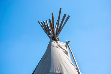 Top of a traditional Native American wigwam lodge or teepee tent against clear blue sky background.  © Evelien