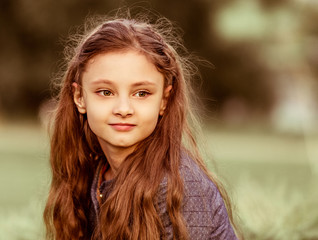 Happy smiling kid girl thinking  with long curly  hair on summer sunset grass background. Closeup