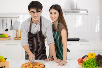 Happy young Asian couple eating Pizza and cooking together homemade pizza.