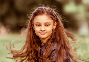Fototapeta premium Happy marvelous smiling kid girl with swirl of incredible curly orange brown long hair on summer grass background. Closeup