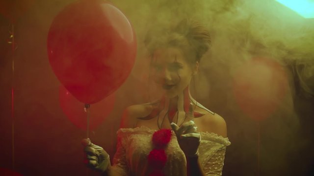 say no, evil clown with bright strange make-up does not want to scream and waves finger, girl with red balloon, masquerade ball for Halloween in white fog. nightmare is watching you, ominous smile