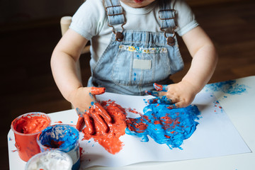Child painting with her hands on the table at home using blue and red paint. Finger painting or art...