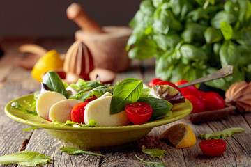 Salad with mozzarella, tomato and basil in green plate on a old wooden background.