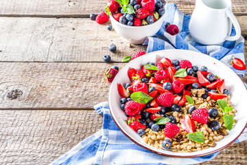 Healthy morning food, Breakfast oatmeal granola or muesli with various berry and milk, yogurt, wooden rustic background. Woman hands hold plate, sppon, flatlay top view