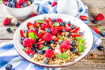 Healthy morning food, Breakfast oatmeal granola or muesli with various berry and milk, yogurt, wooden rustic background. Woman hands hold plate, sppon, flatlay top view