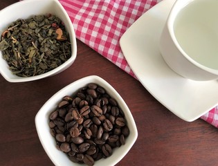 green tea leaves and black coffee beans , white Cup with hot water on a pink tablecloth in the box...