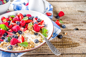 Healthy morning food, Breakfast oatmeal granola or muesli with various berry and milk, yogurt, wooden rustic background. Woman hands hold plate, sppon, flatlay top view