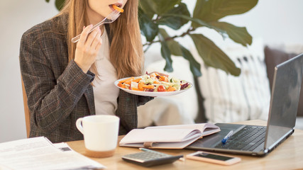 Unrecognizable young business woman having a lunch break at desk, she is eating fresh salad, person