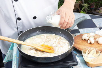 Chef pouring fresh milk the pan for cooking mushroom cream soup