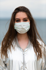 Face portrait of a girl in a medical mask with brown hair and a silver light jacket