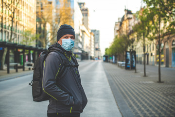 Close up of a Caucasian man, with cap and backpack, and with mask on his face, standing on a deserted street 