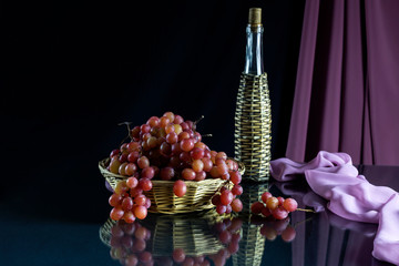 Pink ripe, grapes in a wicker basket, wine in the bottle on the table on a black background close-up
