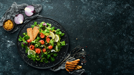 Fresh salad with salmon and olives in black plate. Top view. Free space for your text. Rustic style.