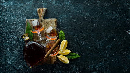 Brandy in glasses and cigars on a black stone table. Top view. Free space for your text.