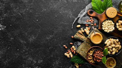 Peanut butter and nuts on a black stone background. Healthy food. Top view.
