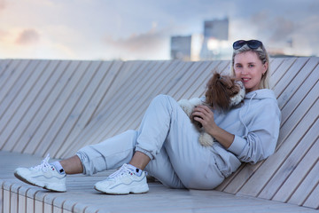 Fototapeta na wymiar Fashionable blonde woman 40 years old in a gray suit walking in the street holding a shih tzu. Fashion spring autumn photo
