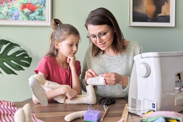 Mother and daughter child together sewing toy hare