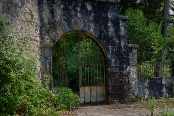 Fototapeta na wymiar Stone fence with iron gates in the trees.