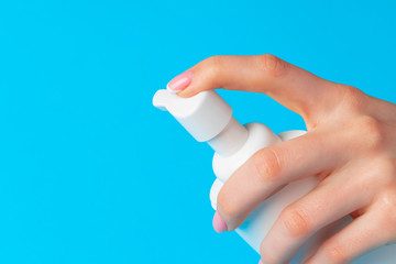 Female hand holding skincare product bottle on blue