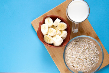 sliced banana slices in a clay plate, a glass mug with milk, a glass bowl with oatmeal. top view