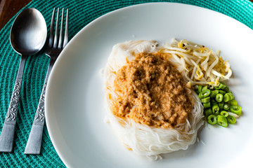 Thai rice noodles with fish curry soup and bean sprout in a white dish on blue table mat.