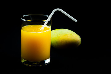 View of mango juice in a glass with a ripe mango on black background.