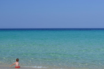 Fototapeta na wymiar Ребенок сидит на берегу и смотрит на море