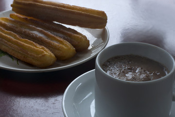 A cup with chocolate and milk and a plate with some traditional spanish churros.