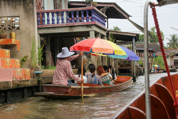 Obraz premium Boat with tourists and a colorful umbrella on the canal of Damnoen Saduak Floating Market in Thailand