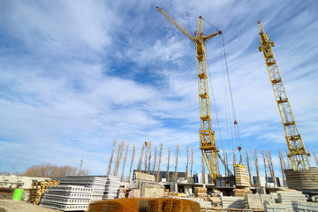 Naklejka premium Photos of high-rise construction cranes and an unfinished house against a blue sky. Photographed on a wide angle lens