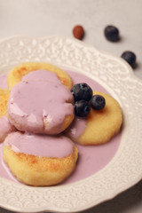 Breakfast of pancakes and yoghurt. Fresh berries and nuts. Blueberries with almonds. Cheesecakes with blueberries and yogurt. Light background. Purple and white