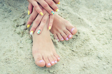 Female hands with manicure and legs with a french pedicure in the sand