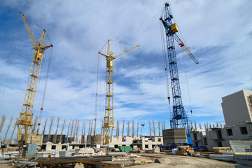 Fototapeta na wymiar Photos of high-rise construction cranes and an unfinished house against a blue sky. Photographed on a wide angle lens