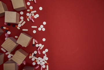 medical pills and wooden cubes scattered on red background