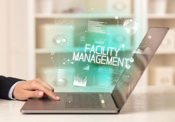 Side view of a business person working on laptop with FACILITY MANAGEMENT inscription, modern business concept